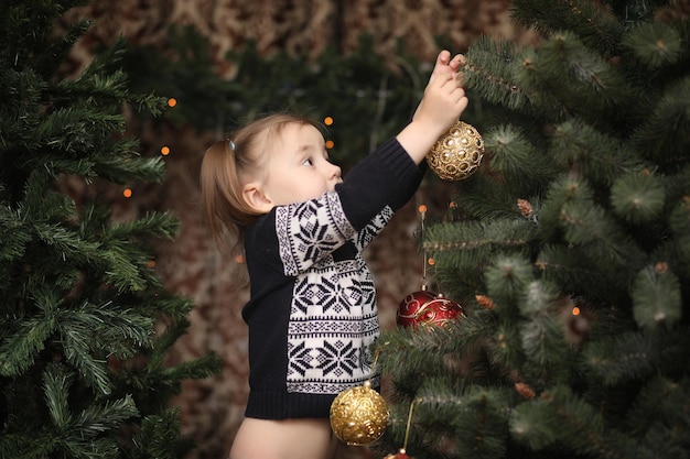 Un niño junto al árbol de Año Nuevo. Los niños decoran el árbol de Navidad. Bebé en un suéter por un árbol verde en estudio.