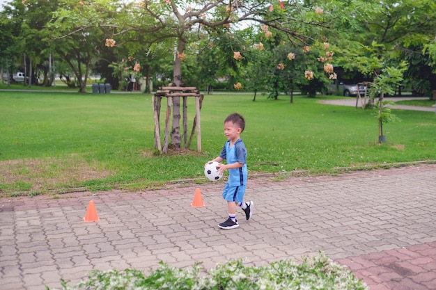 Niño de kindergarten en uniforme de fútbol está jugando fútbol