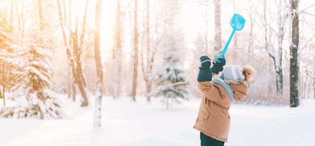 El niño lanza nieve con una pala en el estilo de vida invernal. Paseos de invierno. Un artículo sobre el ocio invernal de los niños.