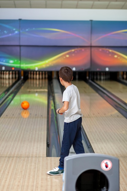 Un niño lanza una pelota a una bolera. Caminos con bolas y bolos para bolos. un juego divertido