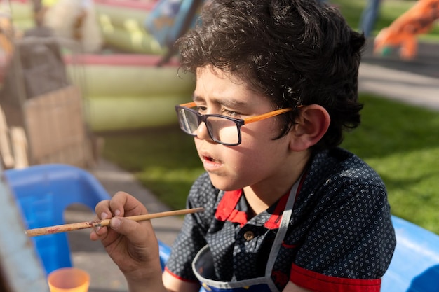 Niño latino pintando en el parque con pinturas y pinceles