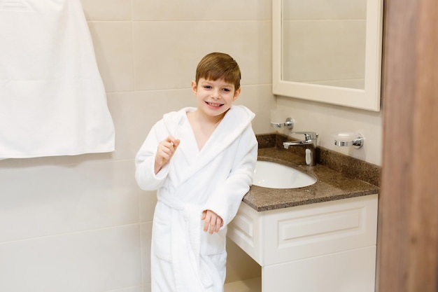 Un niño se lava los dientes en el baño Un niño con bata blanca se lava los dientes