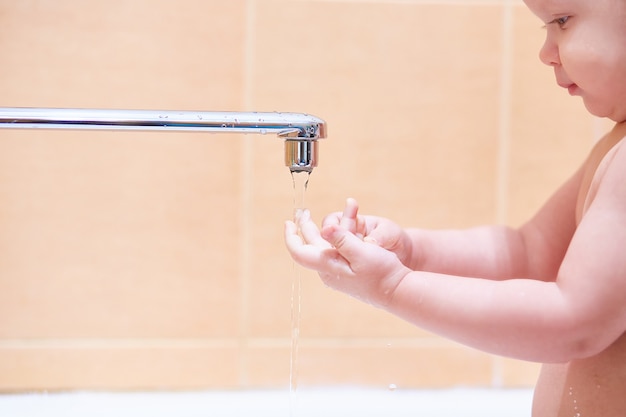 El niño se lava bajo el grifo con agua corriente.