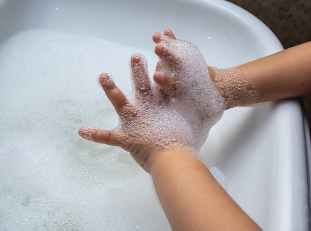 Niño lavando la mano llena de espuma en el lavabo del baño