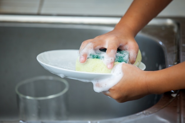 Foto niño lavando los platos sobre el fregadero en la cocina