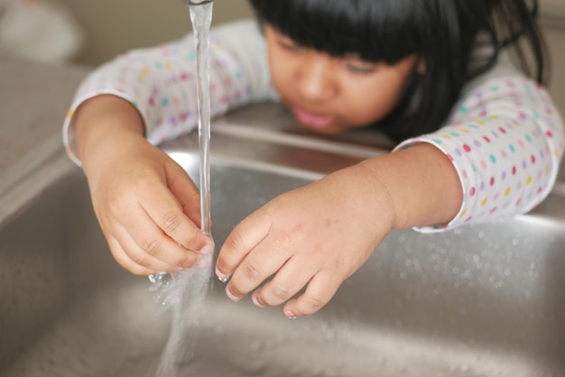 niño lavándose las manos con agua en el fregadero de la cocina