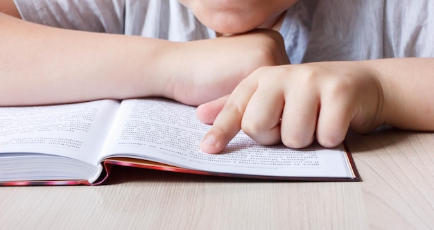 Un niño lee un libro sobre la mesa.