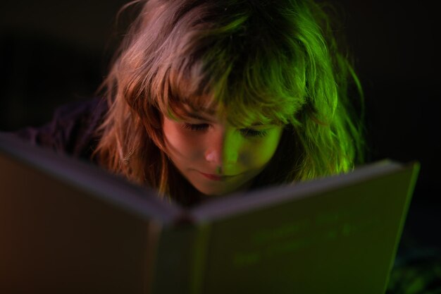 Niño leyendo un cuento antes de dormir en una habitación oscura Un niño lindo leyendo un libro acostado en la cama Niño leyendo un libro en la noche antes de acostarse