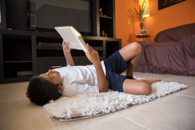 Niño leyendo un libro acostado sobre una estera en casa