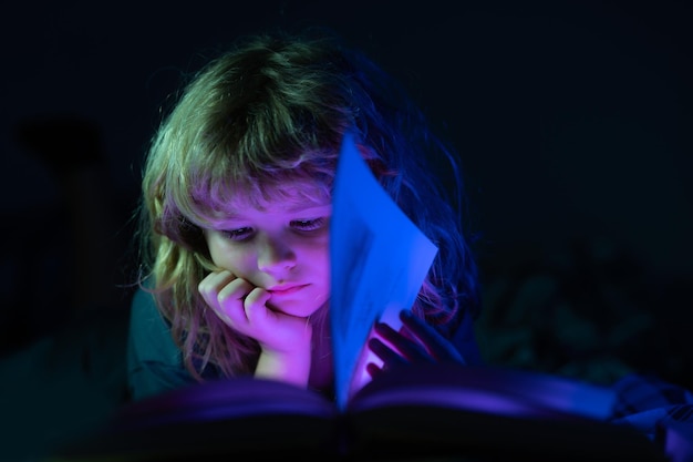 Niño leyendo un libro en la cama antes de ir a dormir niño acostado en la cama leyendo un libro en casa feliz