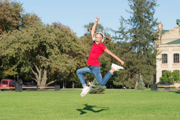 Niño libre y alegre usando tecnología moderna Niño moderno Sonido alto perfecto Chica escuchando música moderno gadget Niño feliz con auriculares inalámbricos bailando corriendo saltando Auriculares estéreo