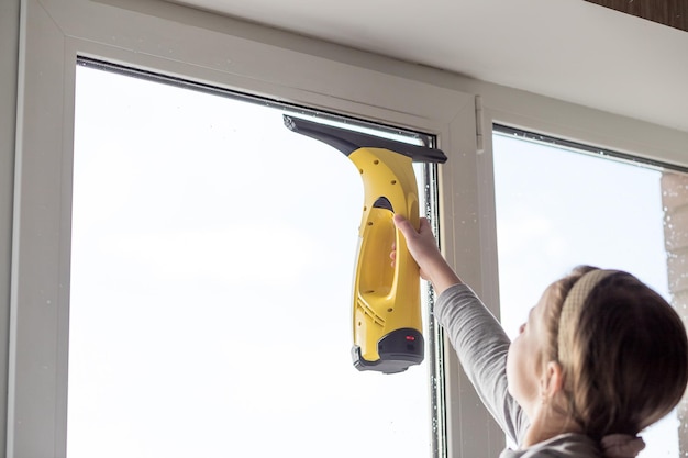 El niño está limpiando el limpiador de ventanas, lavando el vidrio de la  ventana con spray y una aspiradora, la niña lava las ventanas