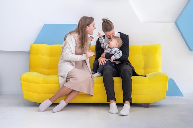 Un niño lindo de 1 año pasa tiempo junto con sus padres en un sofá amarillo