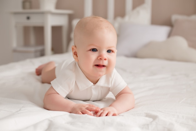 Niño lindo 6 meses yace en la cama sonriendo