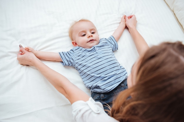 Niño lindo acostado en la cama y jugando con su madre en casa