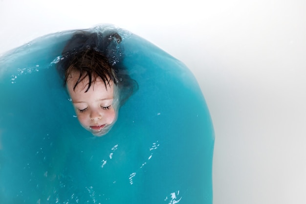 Niño lindo bañándose en agua azul en la bañera