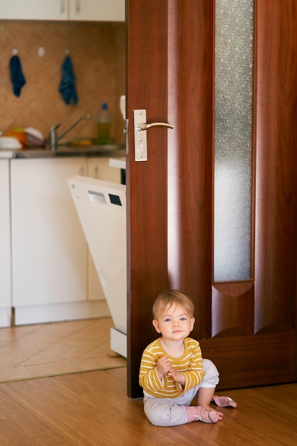 Niño lindo en una blusa de rayas se sienta en el piso de la cocina