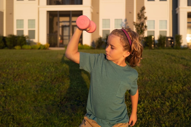 Niño lindo bombeando los músculos del brazo con mancuernas Fitness niños con mancuernas Niños deporte entrenamiento al aire libre