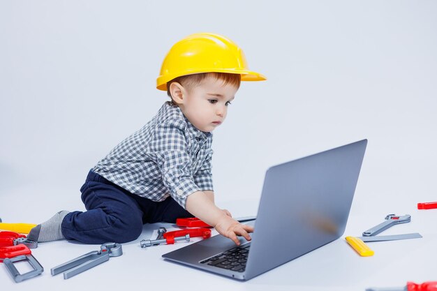 Un niño lindo con una camisa a cuadros se sienta sobre un fondo blanco con una computadora portátil Juguetes para niños