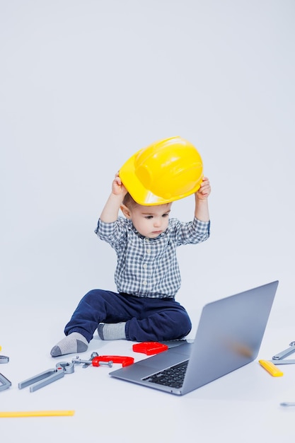 Un niño lindo con una camisa a cuadros se sienta sobre un fondo blanco con una computadora portátil Juguetes para niños