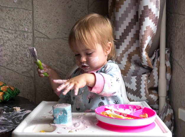 Niño lindo con cara sucia desayunando en casa y sosteniendo un tenedor en la mano