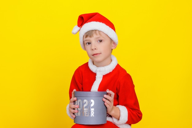 Niño lindo caucásico vestido como Santa Claus sostiene una caja de regalo redonda con el texto Año Nuevo 2022