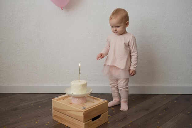 Un niño lindo celebra su cumpleaños con un pastel contra una pared blanca, una niña de rosa es una