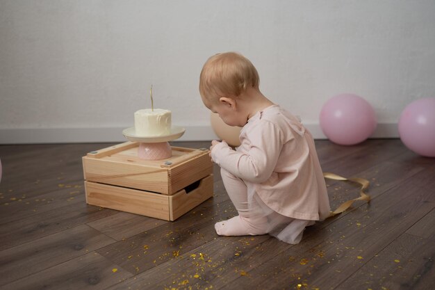 Un niño lindo celebra su cumpleaños con un pastel contra una pared blanca.