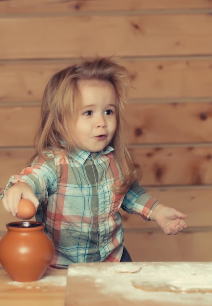 Niño lindo cocinar con masa, harina, huevo y tazón de fuente