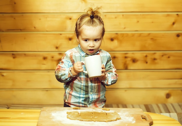 Niño lindo cocinar con masa, harina y taza en madera