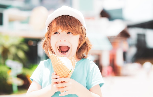 Niño lindo comiendo helado grande lamiendo en cono de gofres feliz riendo en el fondo al aire libre