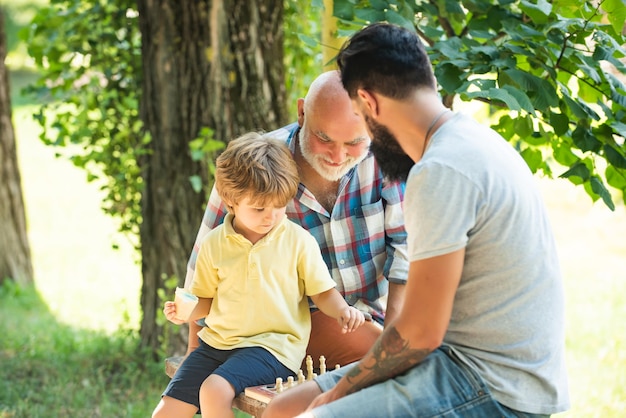 Niño lindo desarrollando estrategia de ajedrez padre hijo y abuelo relajarse juntos edad de oro abuelo...