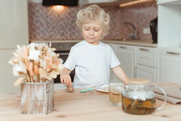Foto un niño lindo está desayunando en la mesa de la cocina. lleva una camiseta blanca.