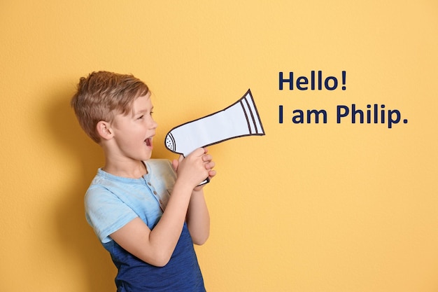 Foto un niño lindo diciendo hola, soy philip usando un megáfono de papel con fondo amarillo