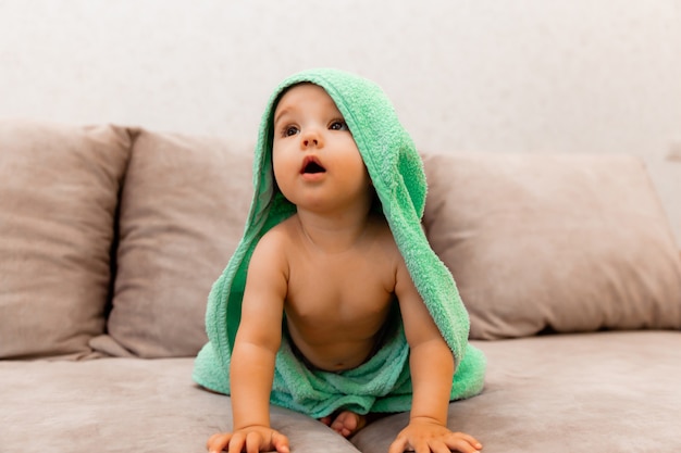 Un niño lindo envuelto en una toalla se sienta en la cama. bebé en una toalla de baño.
