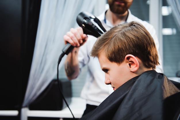 Niño lindo es corte de pelo por peluquero en la barbería.