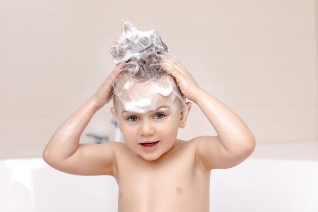 Niño lindo con espuma de champú en la cabeza, tomar un baño y lavarse el cabello