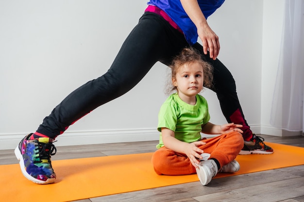 Un niño lindo está aburrido mientras su madre hace yoga por la mañana