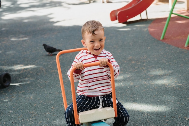 Un niño lindo se está divirtiendo en el patio de recreo montado en un columpio