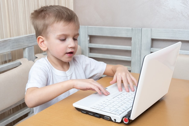 Un niño lindo está sentado en una mesa y está escribiendo la tarea en una computadora portátil en casa. Concepto de aprendizaje, aprendizaje a distancia, autoeducación, lección de videoconferencia con mentor