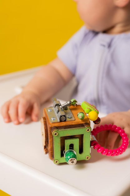 Un niño lindo está sentado en una silla para niños jugando con un juguete educativo de madera en un biziboard de fondo amarillo