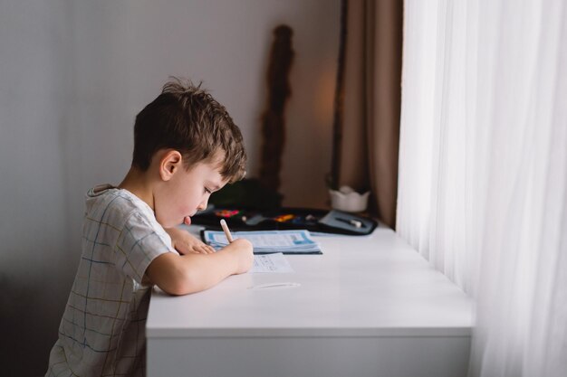 Niño lindo estudiando en casa y haciendo la tarea de la escuela pensando en un niño sentado en la mesa