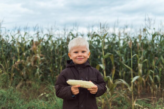 Foto niño lindo y feliz en el campo de maíz sosteniendo el maíz