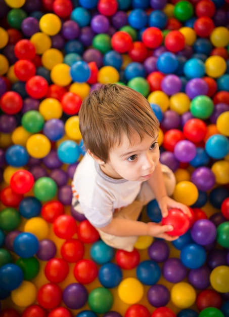 Niño lindo feliz jugando y divirtiéndose en el jardín de la infancia con bolas de colores