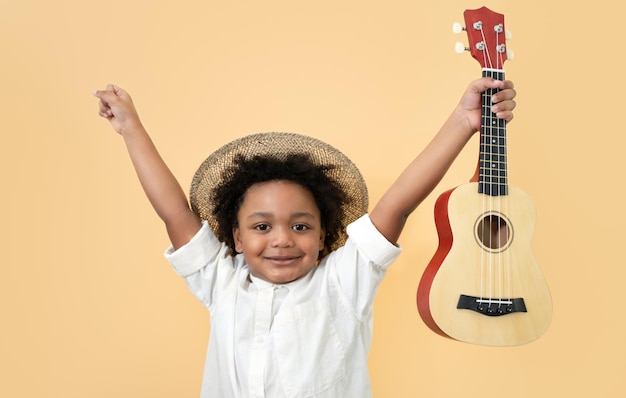 Niño lindo feliz con pelo afro y ukelele sobre fondo amarillo