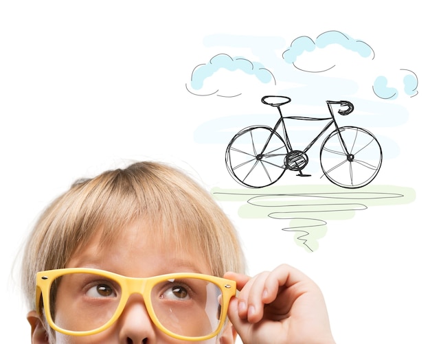 Un niño lindo con gafas amarillas soñando con una bicicleta