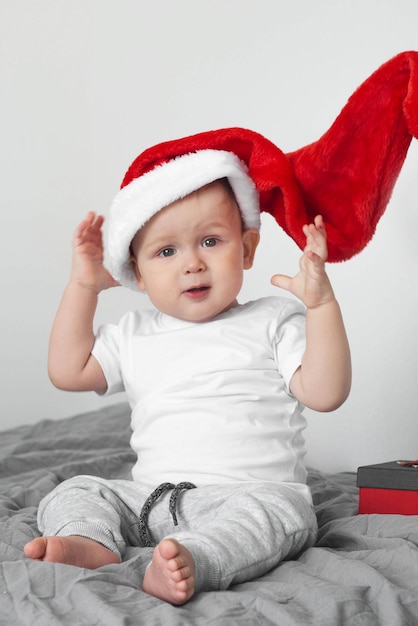 Niño lindo con gorro de Papá Noel sentado en la cama