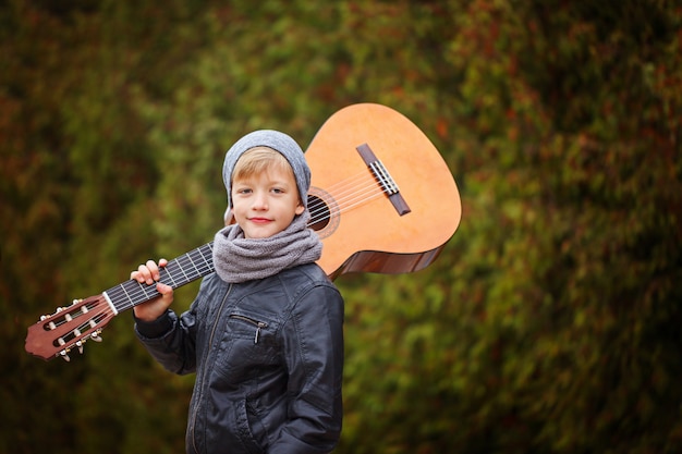 Niño lindo con guitarra en la naturaleza