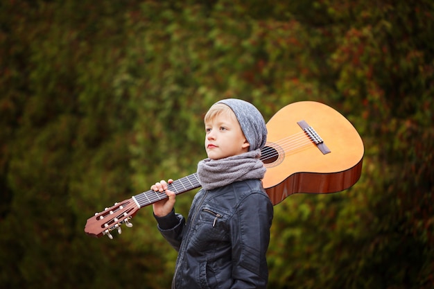 Niño lindo con guitarra en la naturaleza