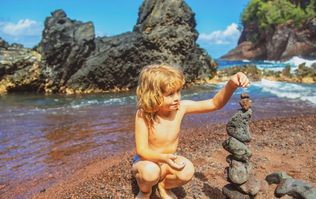 Un niño lindo haciendo guijarros se apilan en una roca volcánica junto al concepto zen del mar